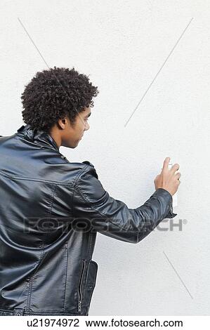 Stock Image - Man holding spray paint against white wall, studio shot. Fotosearch