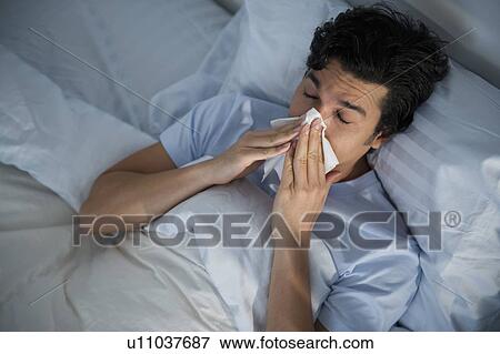 Stock Photo - Man lying in bed and blowing nose. Fotosearch