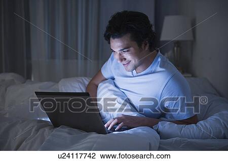 Stock Image - Man using laptop in bed. Fotosearch