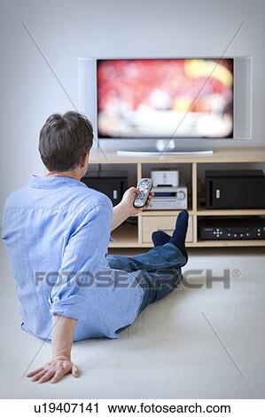 Stock Image - Man watching tv in living room. Fotosearch