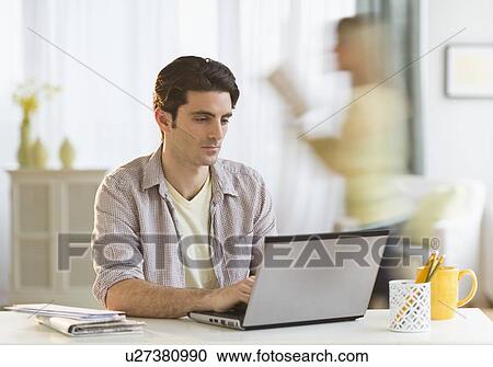 Man working on laptop at home, woman in background View Large Photo Image Stock Image - Man working on laptop at home, woman in background. Fotosearch