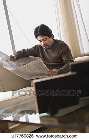 Stock Photograph - Mature man reading newspaper in living room. Fotosearch
