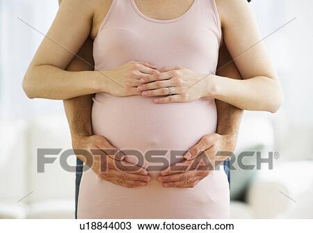 Stock Image - Midsection of man hugging pregnant woman. Fotosearch