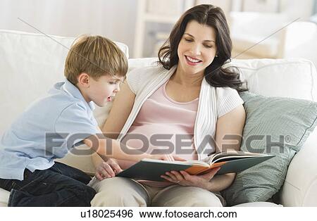 Stock Photograph - Mother and son (4-5) reading book on sofa. Fotosearch