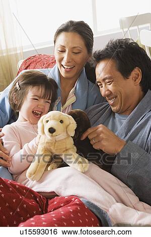 Parents and daughter sitting in bed and playing with stuffed toys View Large Photo Image Stock Photograph - Parents and daughter sitting in bed and playing with stuffed toys. Fotosearch