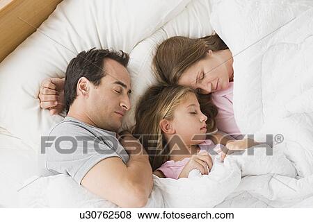 Stock Photo - Parents with daughter (12-13) sleeping in bed. Fotosearch