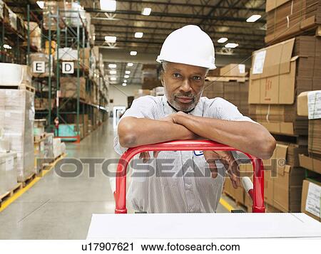 Portrait of man pushing hand truck in warehouse View Large Photo Image Stock Image - Portrait of man pushing hand truck in warehouse. Fotosearch