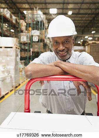 Stock Photograph - Portrait of man pushing hand truck in warehouse. Fotosearch