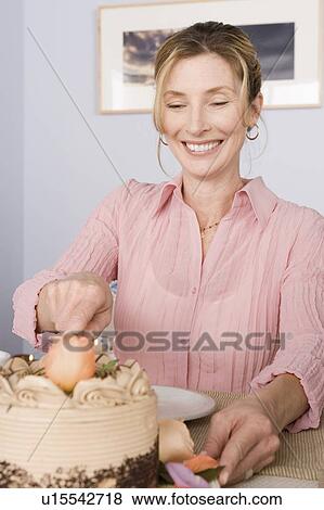 Stock Photo - Portrait of mature woman cutting cake. Fotosearch