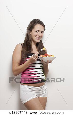 Stock Image - Portrait of pregnant woman holding bowl with salad, studio shot. Fotosearch