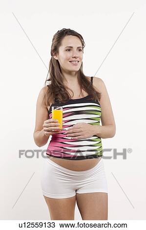 Stock Image - Portrait of pregnant woman holding glass of orange juice, studio shot. Fotosearch