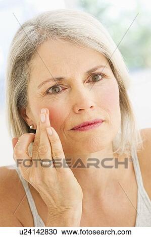 Stock Image - Portrait of senior woman applying moisturizer. Fotosearch