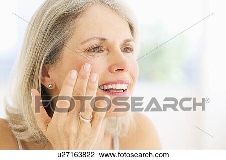 Stock Image - Portrait of senior woman applying moisturizer. Fotosearch