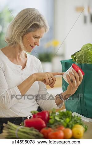 Stock Photo - Portrait of senior woman checking product in kitchen. Fotosearch