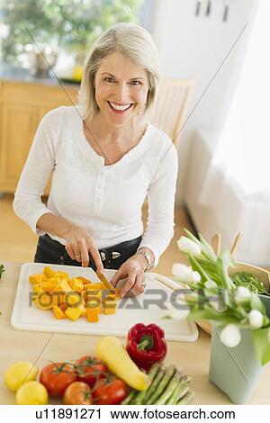 Stock Image - Portrait of senior woman cutting vegetables in kitchen. Fotosearch