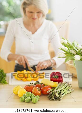 Stock Image - Portrait of senior woman cutting vegetables in kitchen. Fotosearch