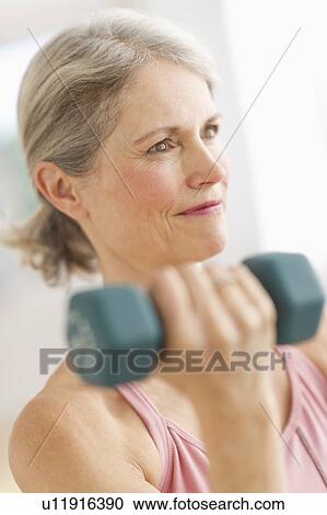 Stock Image - Portrait of senior woman exercising with dumbbells in gym. Fotosearch