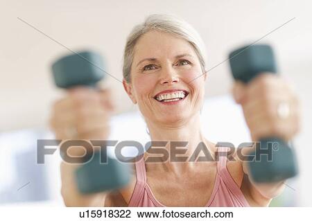 Stock Image - Portrait of senior woman exercising with dumbbells in gym. Fotosearch