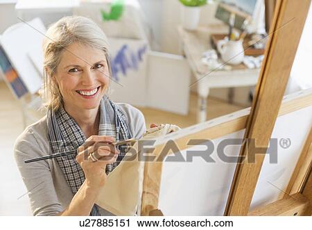 Stock Image - Portrait of senior woman painting on canvas. Fotosearch