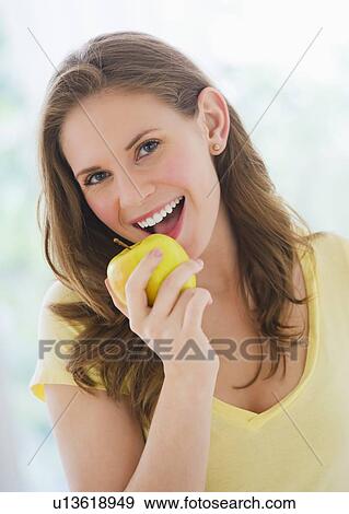 Stock Photo - Portrait of smiling young woman holding apple. Fotosearch