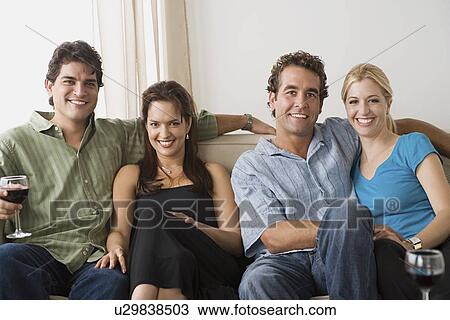 Stock Image - Portrait of two smiling couples sitting on sofa. Fotosearch
