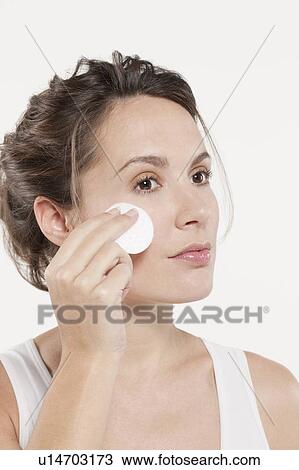 Stock Image - Portrait of woman touching face with cotton pad, studio shot. Fotosearch