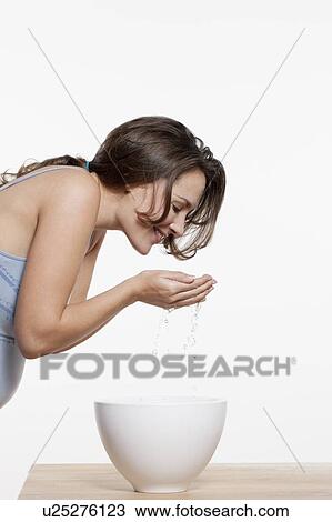 Stock Image - Portrait of woman washing face, studio shot. Fotosearch