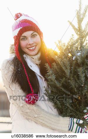 Stock Photograph - Portrait of young woman carrying Christms tree. Fotosearch