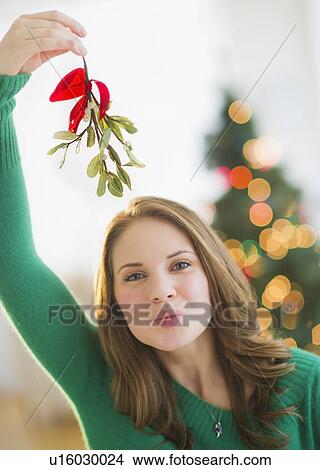 Portrait of young woman holding mistletoe stem over head View Large Photo Image Picture - Portrait of young woman holding mistletoe stem over head. Fotosearch