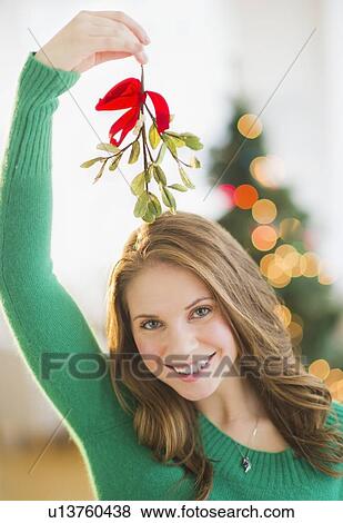 Stock Photo - Portrait of young woman holding mistletoe stem over head. Fotosearch