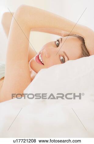 Stock Photo - Portrait of young woman lying on bed in bedroom. Fotosearch