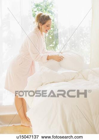 Stock Photo - Portrait of young woman making bed. Fotosearch