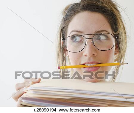 Portrait of young woman wearing glasses and holding pencil in mouth, studio shot View Large Photo Image Picture - Portrait of young woman wearing glasses and holding pencil in mouth, studio shot. Fotosearch