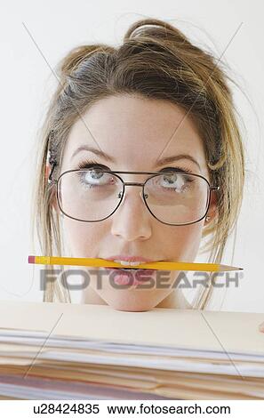 Portrait of young woman wearing glasses and holding pencil in mouth, studio shot View Large Photo Image Stock Photography - Portrait of young woman wearing glasses and holding pencil in mouth, studio shot. Fotosearch