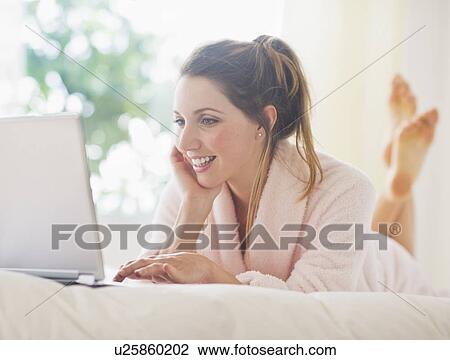 Stock Image - Portrait of young woman with laptop in bedroom. Fotosearch