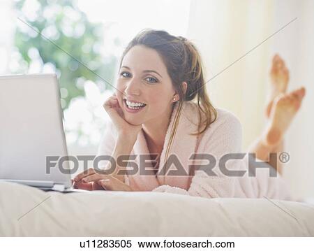 Stock Photography - Portrait of young woman with laptop in bedroom. Fotosearch