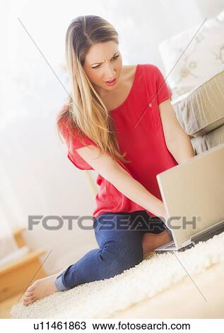 Stock Image - Portrait of young woman working with laptop in living room. Fotosearch