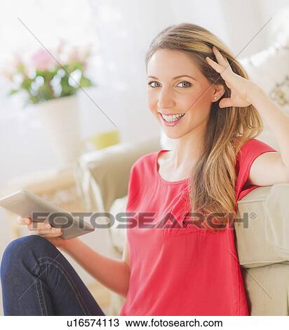 Stock Image - Portrait of young woman working with digital tablet in living room. Fotosearch