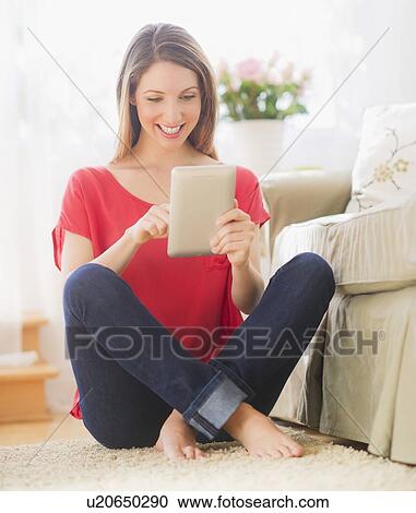 Stock Image - Portrait of young woman working with digital tablet in living room. Fotosearch