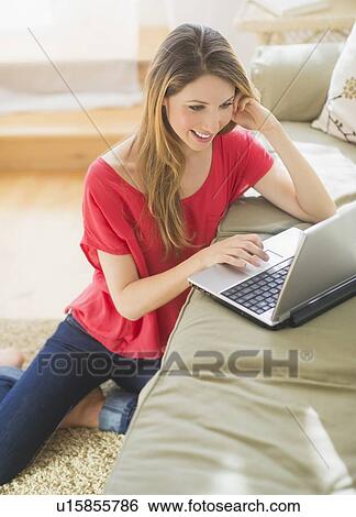 Stock Photograph - Portrait of young woman working with laptop in living room. Fotosearch