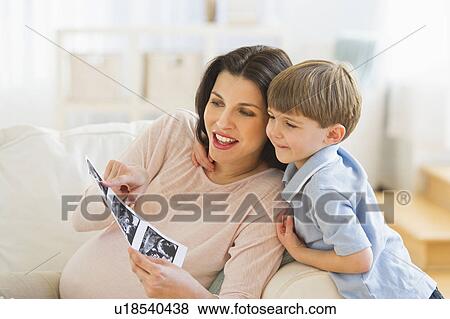 Stock Photo - Pregnant woman with son (4-5) looking at ultrasound photo. Fotosearch