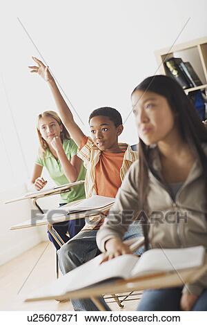 Stock Image - School children rising hands in classroom . Fotosearch