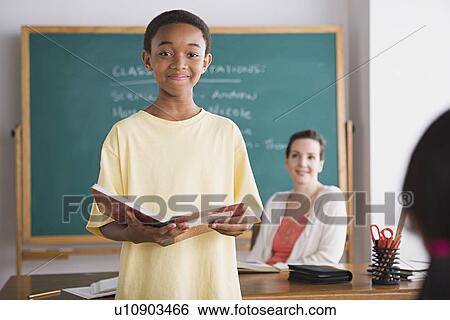 Schoolboy posing with book, teacher in background View Large Photo Image Stock Photograph - Schoolboy posing with book, teacher in background. Fotosearch