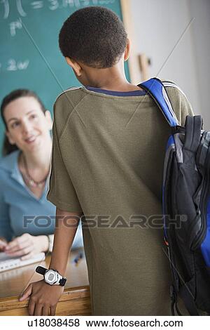 Stock Photo - Schoolboy talking to teacher sitting behind desk. Fotosearch