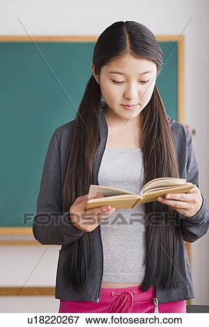 Stock Photo - Schoolgirl reading book in front of blackboard. Fotosearch