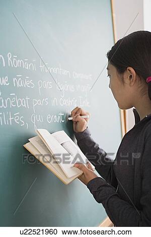 Schoolgirl writing on blackboard while holding book in her hand View Large Photo Image Stock Image - Schoolgirl writing on blackboard while holding book in her hand. Fotosearch