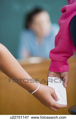 Stock Photo - Schoolgirls passing crib one to another during test. Fotosearch