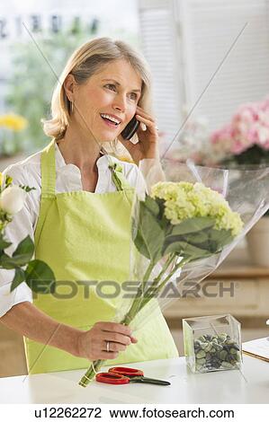 Stock Image - Senior female florist talking on mobile phone. Fotosearch