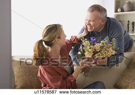 Senior man giving flowers to woman sitting on sofa View Large Photo Image Stock Photo - Senior man giving flowers to woman sitting on sofa. Fotosearch