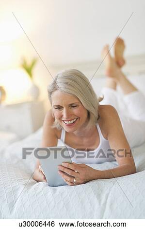 Senior woman lying on bed and using digital tablet View Large Photo Image Stock Photograph - Senior woman lying on bed and using digital tablet. Fotosearch
